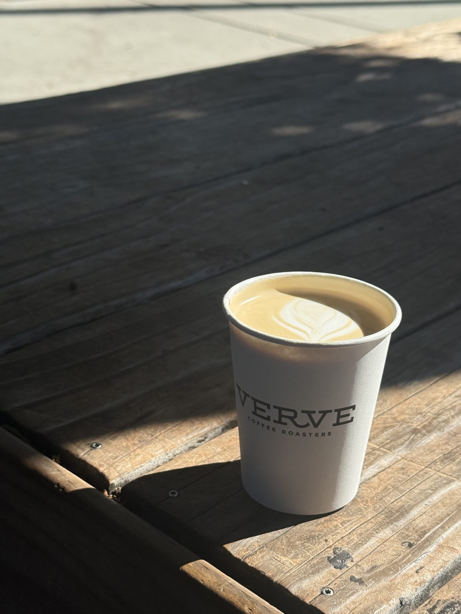 A Verve Coffee latte with latte art sitting on a sunlit wooden bench