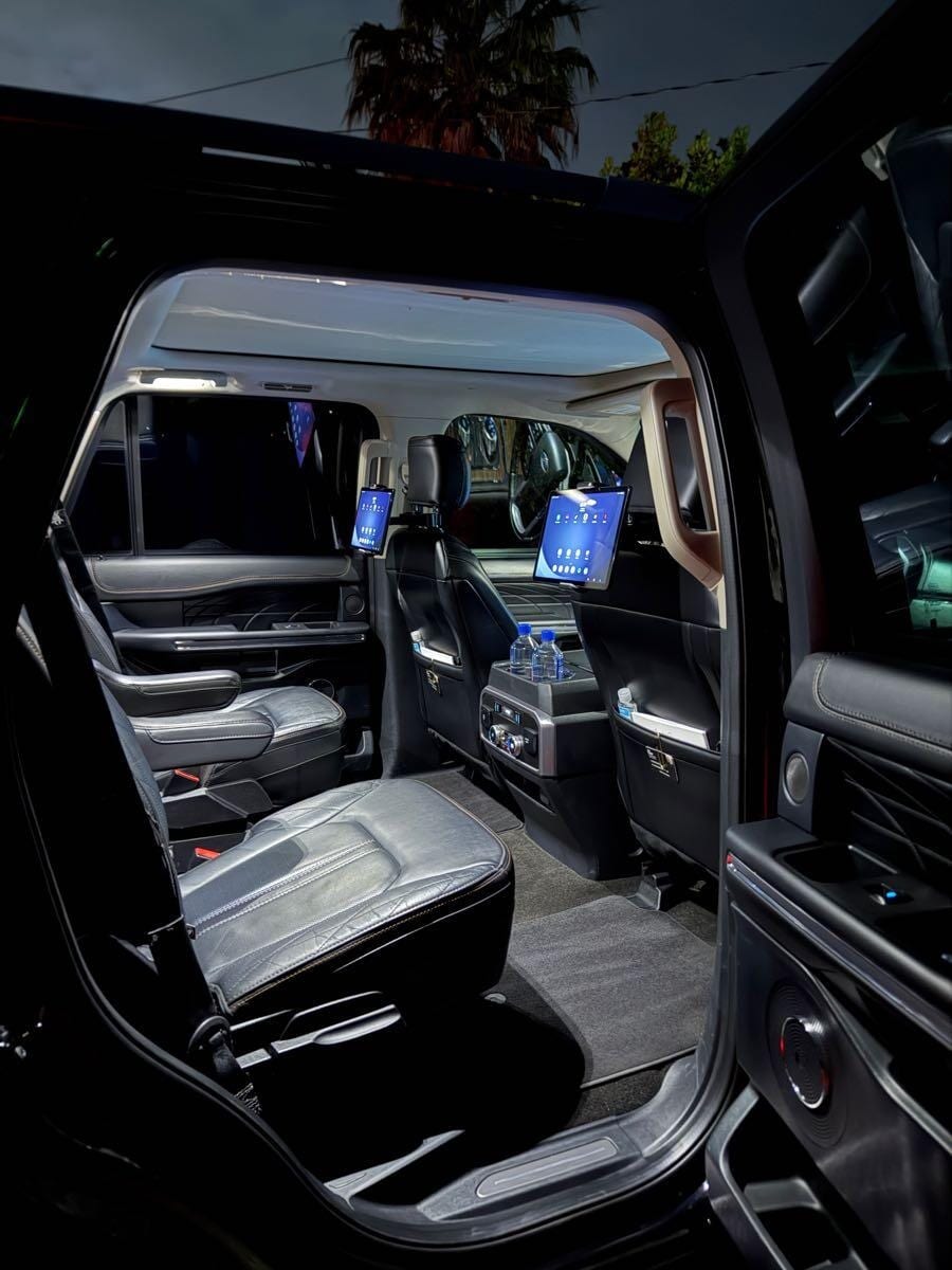 Lit rear cabin of the SUV with captain's chairs, seatback tablets and bottled water
