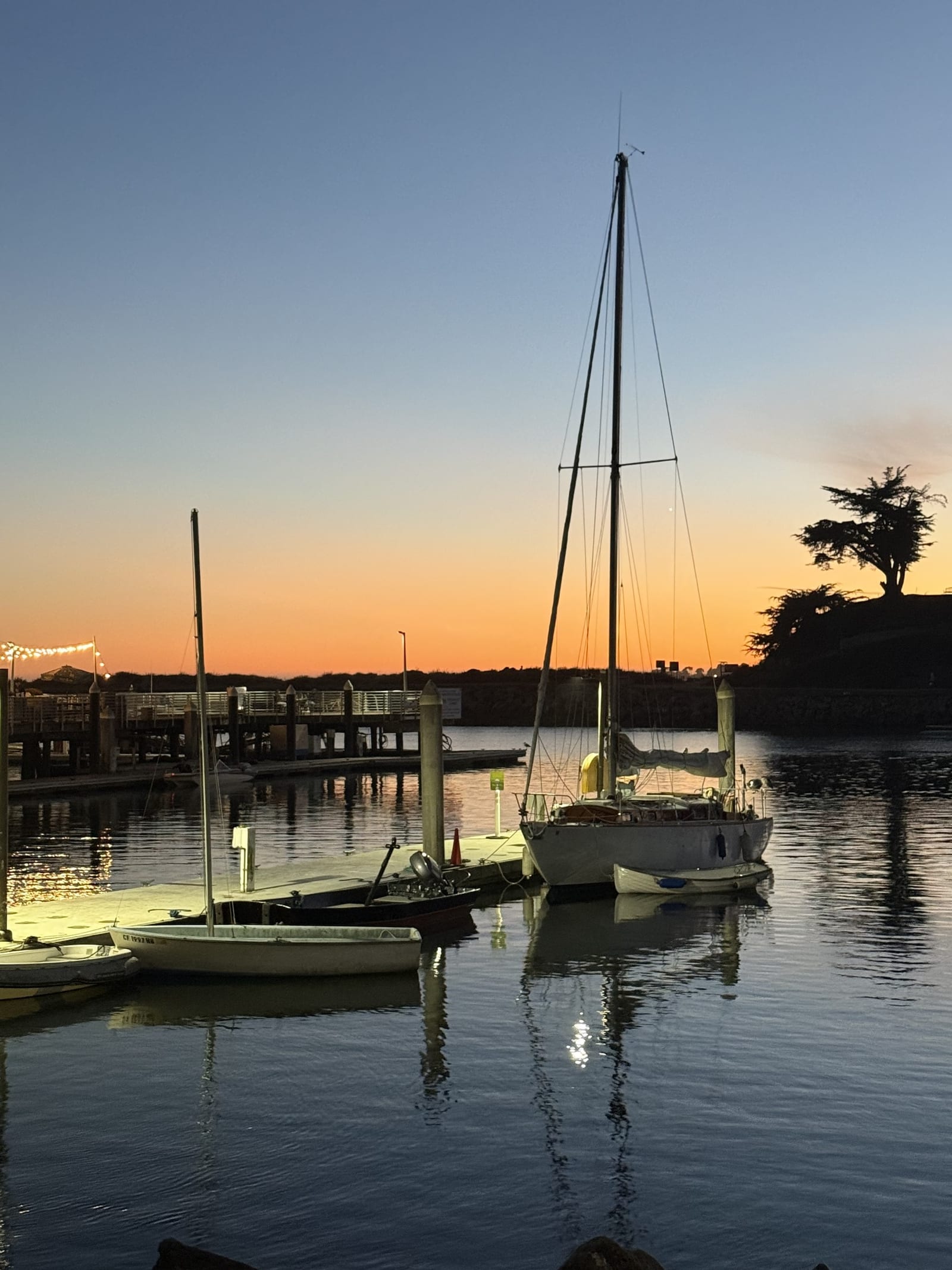 Sailboats docked in the Santa Cruz harbor at dusk under an orange sky